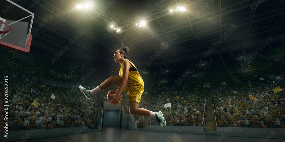 Wall mural Female basketball player makes slam dunk. Basketball player on big professional arena during the game