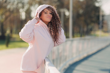 Young happy attractive woman posing on a fence near a running track