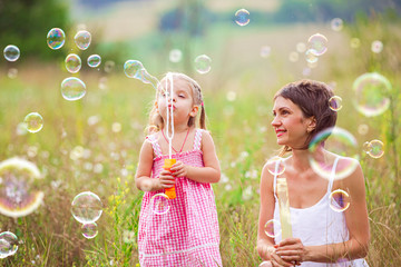 Mother and little girl daughter child blowing soap bubbles outdoor. Parent and kid having fun on...