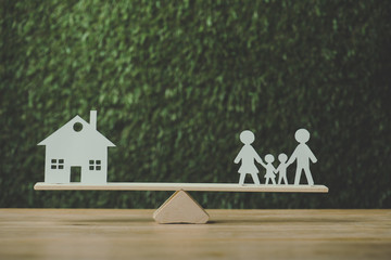 paper cut house and paper family balancing on seesaw on green background