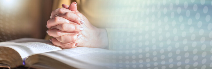 Woman praying with her hands over the bible, hard light; panoramic banner