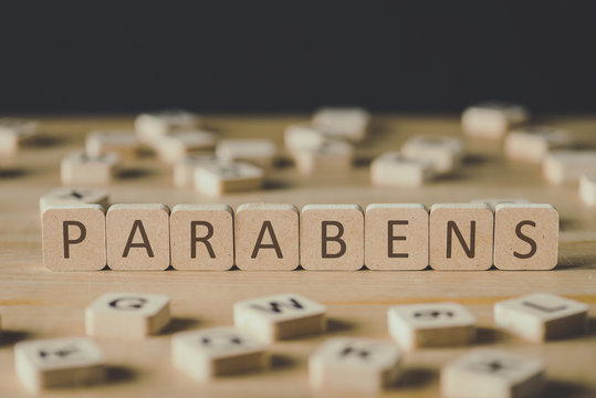 selective focus of word parabens made of cubes surrounded by blocks with letters on wooden surface isolated on black