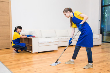 professional cleaning service. Two women in working uniform, in aprons, divide the cleaning of the kitchen of a private house, cottage. Washing floor