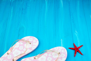 Pink with white flowers flip flop sandals beach shoes on blue wooden floor. Top view and copy space.