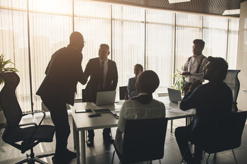 Silhouettes of people sitting at the table. A team of young businessmen working and communicating together in an office. Corporate businessteam and manager in a meeting.