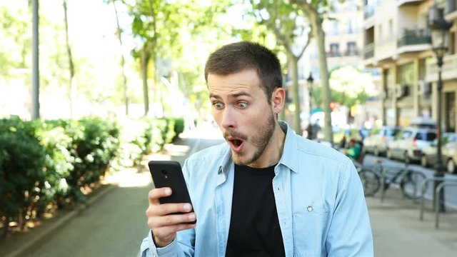 Amazed man using smart phone and looks at camera in the street