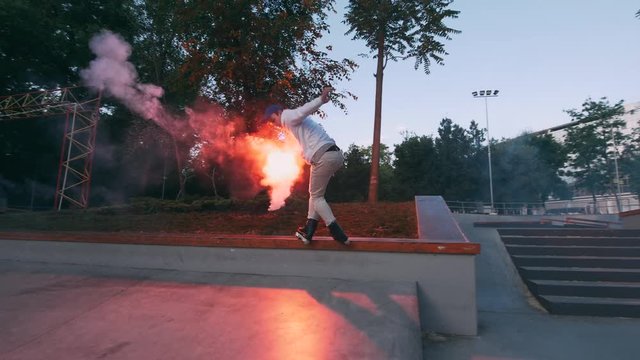 Aggressive Inline roller skater doing tricks in concrete skatepark with red burning signal flare outdoors, slow motion