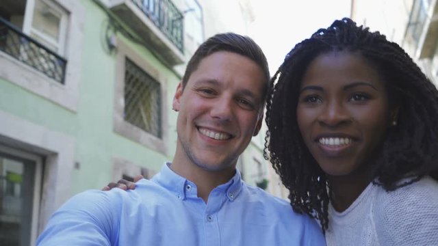 Happy multiracial couple posing for self portrait outdoor. Handsome Caucasian man posing with beautiful African American woman who blowing air kisses. Concept of self portrait