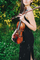 beautiful girl holding a violin in her hands. violinist in the forest