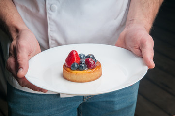 Obraz na płótnie Canvas Restaurant chef holding plate with sweet dessert. Close-up of unrecognizable male cook showing refreshing dessert. Bakery cafe concept