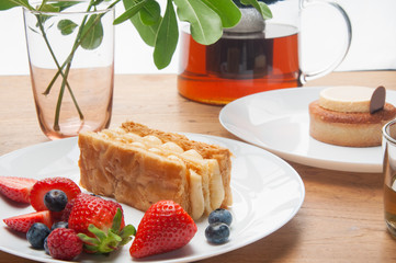 Closeup of cakes portions, fresh berries and teapot on table. Delicious pastries, teapot with tea...