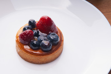 Closeup of delicious mini tart with berries on plate. Beautiful pastry with strawberries and blueberries on table. Dessert concept.
