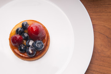 Closeup of delicious mini tart with berries on white plate. Beautiful pastry with strawberries and blueberries on table. Dessert concept. Top view.