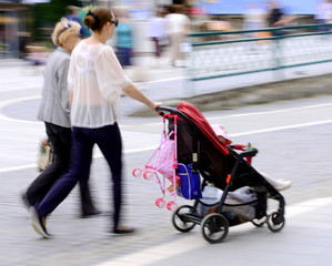 Young mother with small child in the stroller walking down the s