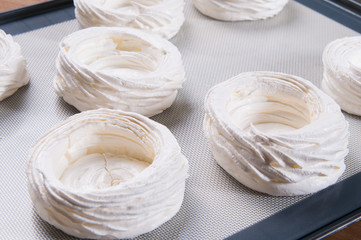 Closeup of white meringue nests on tray. Delicious cookies. Pastry cooking or confection concept.