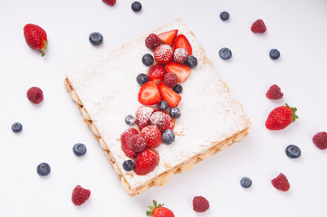 Above view of flaky berry cake with powder sugar topping. Puff pastry dessert surrounded by berries. Cooking concept