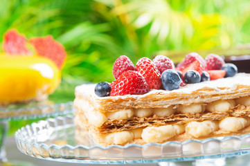 Close-up of crispy cake with cream and berries on stand. Beautiful fresh cake outdoors. Candy bar concept