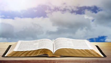 Open book on old wooden table on sky background sunlit