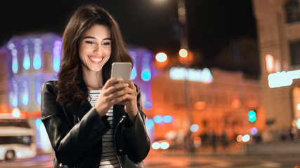 Girl sending message on phone, walking in city at night