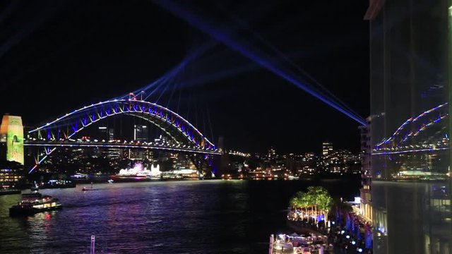 Arch of Sydney Harbour bridge and light show reflecting in glass during Vivid Sydney light show.