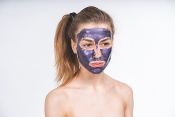 emotional portrait of a young beautiful european girl in violet cosmetic mask on her face. European, 22 years old, white, empty background