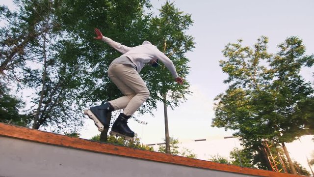 Aggressive Inline roller skater doing tricks in concrete skatepark outdoors, slow motion, low angle view