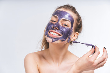 young girl with beautiful face removes a purple cosmetic mask. Close-up. Macro. Smile, joy. White beautiful teeth