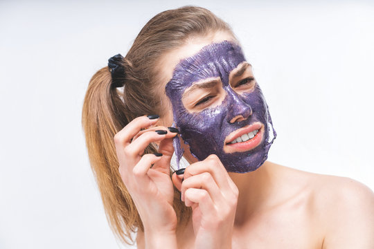 A Young Girl With A Beautiful Face With Difficulty Removes A Purple Cosmetic Mask. Close-up. Macro. Pain, Irritation. Facial Care