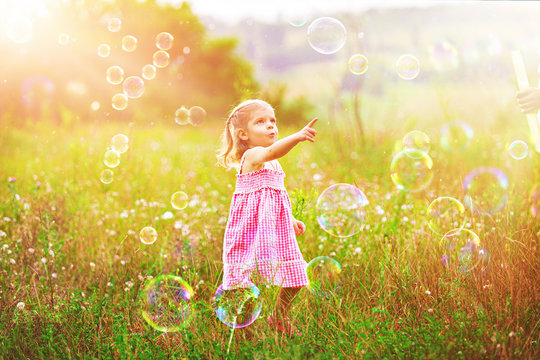 Funny little girl catching soap bubbles in the summer on nature. Happy childhood concept.