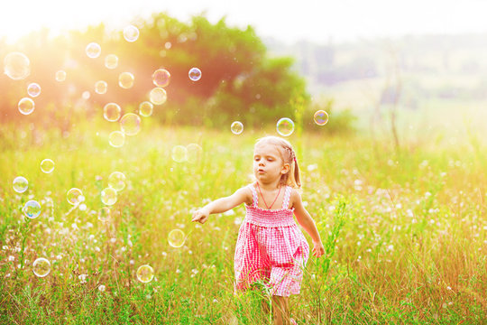 Funny little girl catching soap bubbles in the summer on nature. Happy childhood concept.