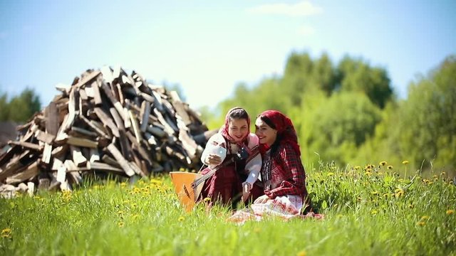 Two young women in traditional russian clothes sitting on the field and taking a selfie