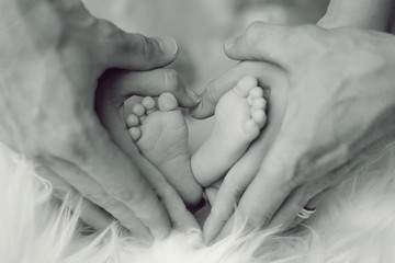 Babyfüße mit den Händen der Eltern als Herz geformt