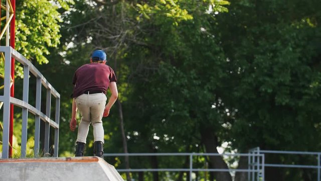 Aggressive Inline roller skater doing tricks in concrete skatepark outdoors with beautiful background, super slow motion