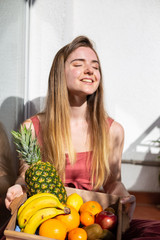 Obraz premium Happy young beautiful female in casual summer dress sitting on balcony with bowl with ripe tropical fruits