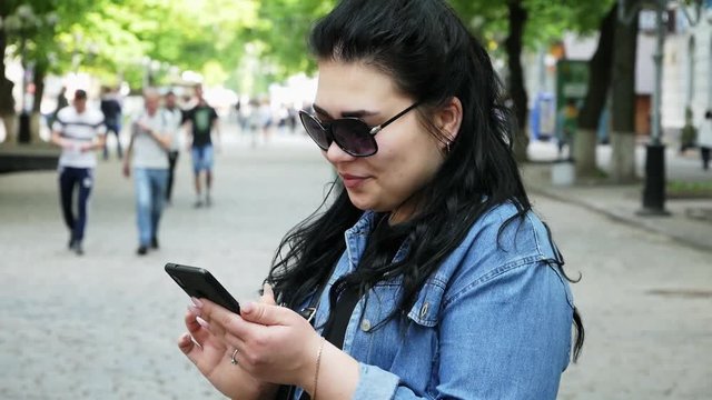 Young successful woman uses a mobile phone on the street, people on background