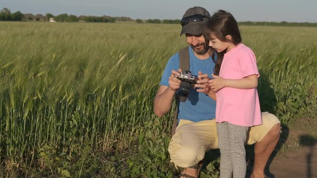 Family with a camera in nature. A father teaches his little daughter to take pictures in nature.