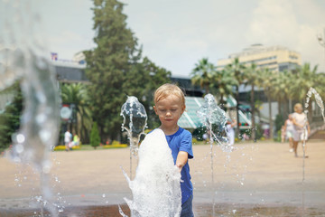 A boy playing with water in park fountain. Hot summer. Happy young boy has fun playing in water fountains