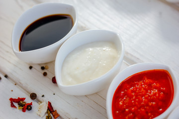 Different dips and sauces - red, white and black over white table.