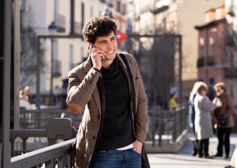 Young attractive happy man talking on smart phone in european city