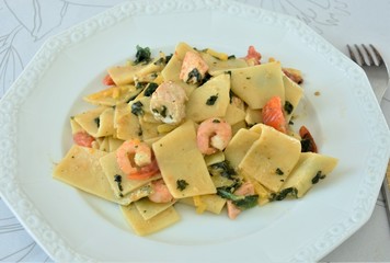 noodles with fish, shrimps and spinach on a white plate