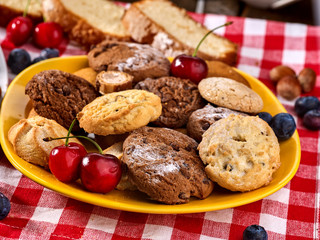 Chocolate oatmeal cookies and sand heart shape cake with blueberries on table in farm style. Table setting breakfast on gingham tablecloth.