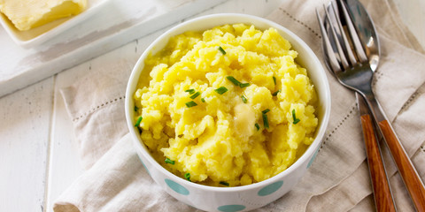Mashed potatoes in bowl with butter and milk on white wooden rustic table. Free space for your text.