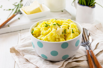 Mashed potatoes in bowl with butter and milkon white wooden rustic table.