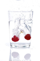 high-speed photograph of two red cherries falling into a glass of water causing splashes on white background