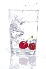 high-speed photograph of two red cherries falling into a glass of water causing splashes on white background