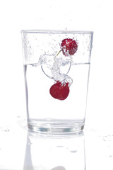 high-speed photograph of two red cherries falling into a glass of water causing splashes on white background