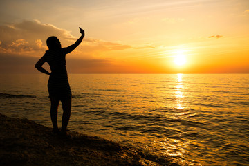 Fototapeta premium silhouette of a young girl. makes selfie at sea sunset.