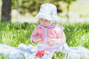 Child sitting on the blanket on the green grass, summer time, outdoors
