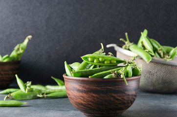 Closeup of fresh green peas in the rural bowl on the gray table against dark background