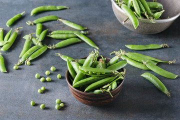 Fresh picked peas in pods.Bowl with peas on the grey table.Fresh spring harvest of sweet peas